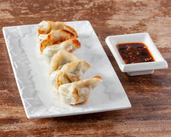 Six raviolis grillés dorés, alignés sur une assiette blanche, avec une coupelle de sauce pimentée