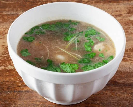 Un bol de soupe de raviolis au bouillon clair, parsemé de coriandre