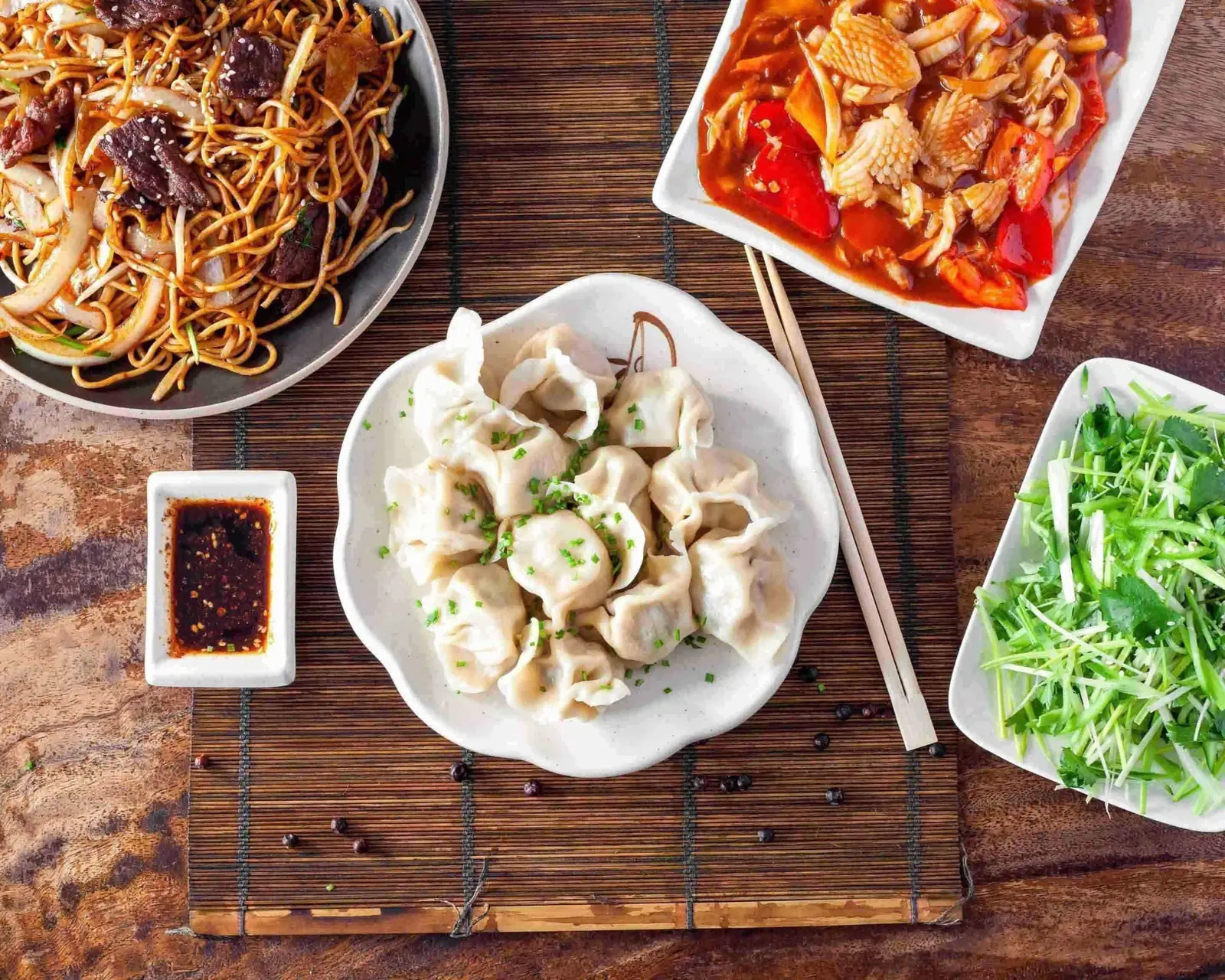 Une table dressée : raviolis en bouillon, nouilles sautées, salade et sauce pimentée