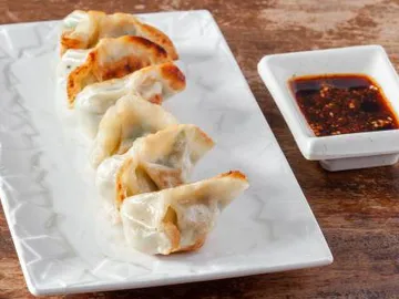 Six raviolis grillés dorés sur une assiette, avec une coupelle de sauce
